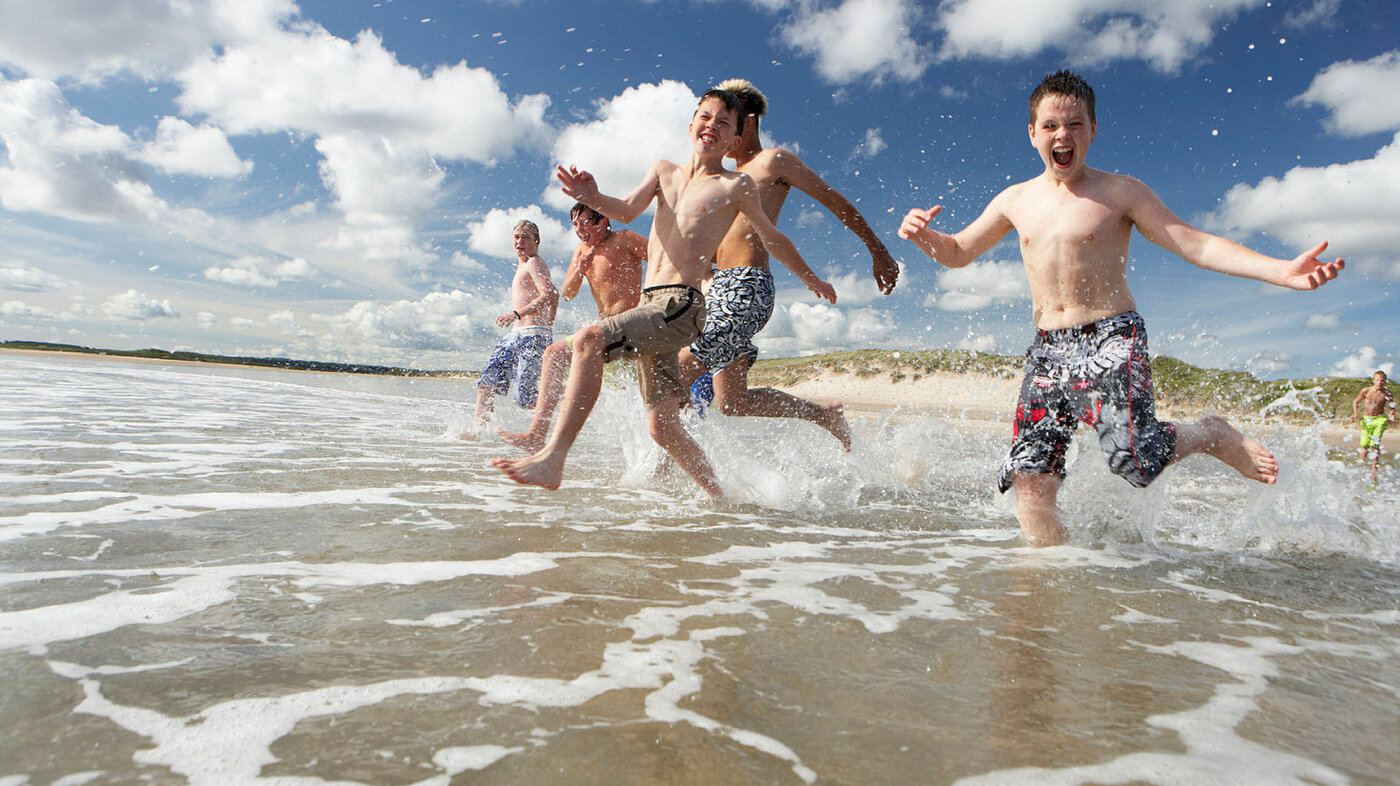 Bildet viser en gjeng med gutter som løper ut i vannet på en strand