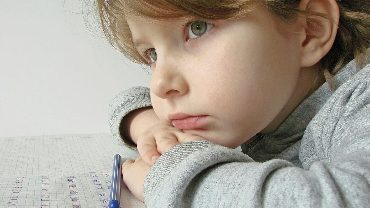 Bildet viser en tankefull jente som øver på å skrive bokstaver på et papir.