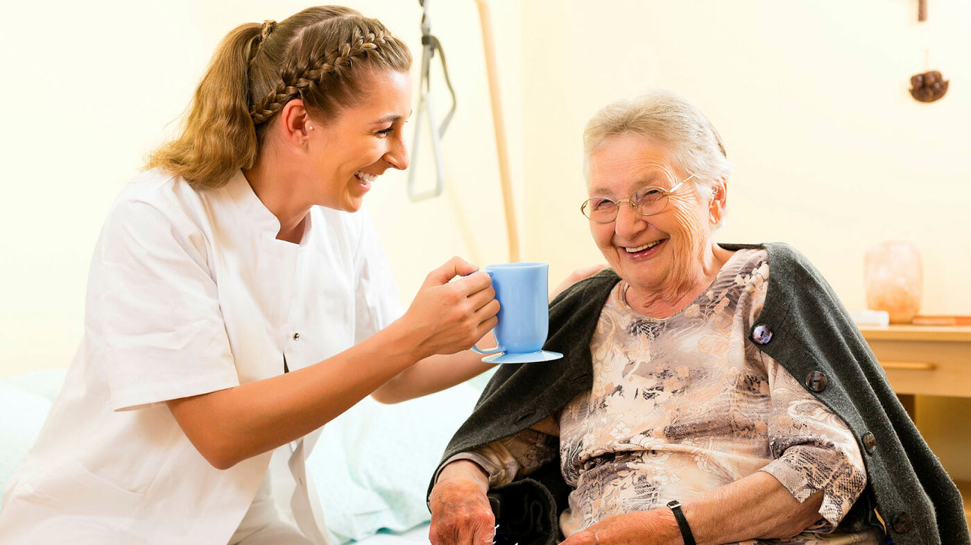Bildet viser en pleier som serverer kaffe til en eldre dame/pasient.