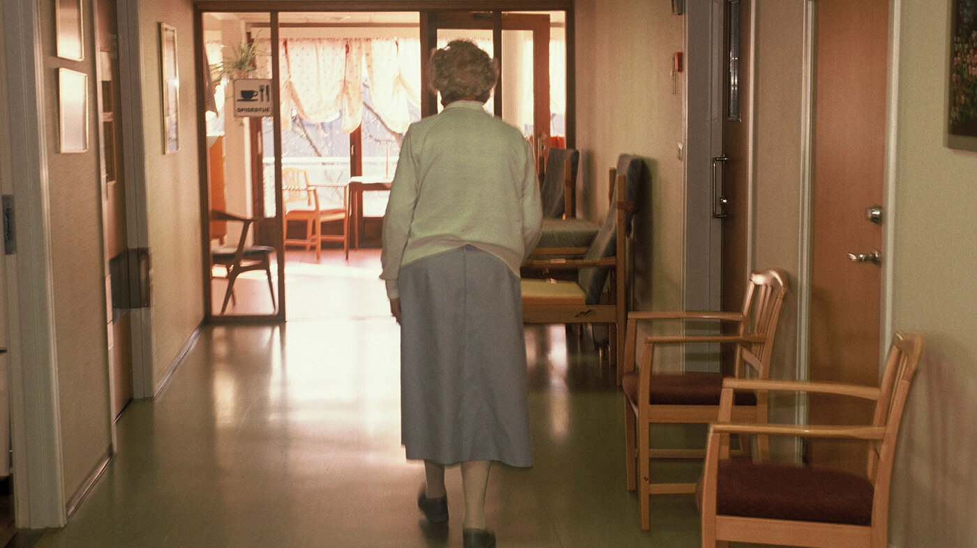 Eldre kvinne går nedover sykehjemskorridor