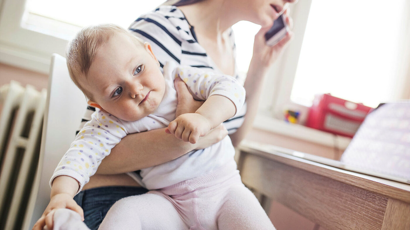 Bildet viser en mor som er mer opptatt av mobiltelefonen enn barnet.