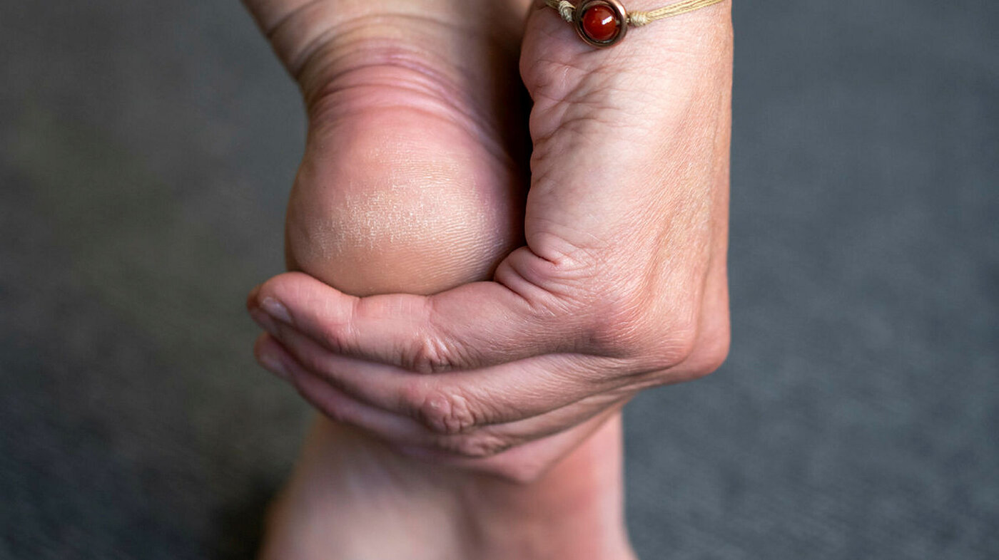 Bildet viser en hånd som rører en fot med smerter.