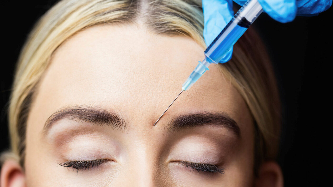 Woman receiving botox injection on her forehead in a examination room