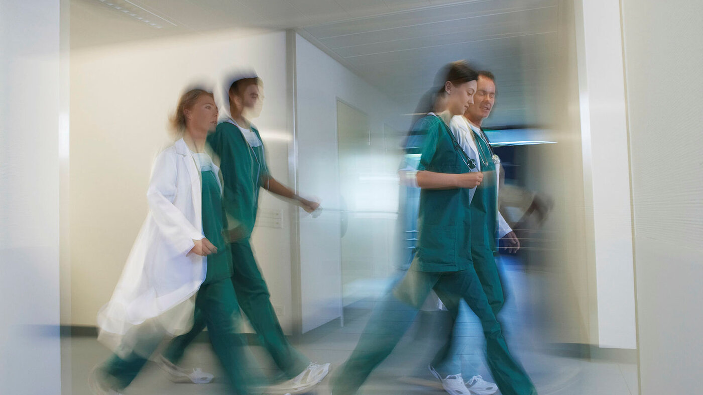 Bildet viser fire sykepleiere som går raskt gjennom en gang, på et uskarpt bilde.