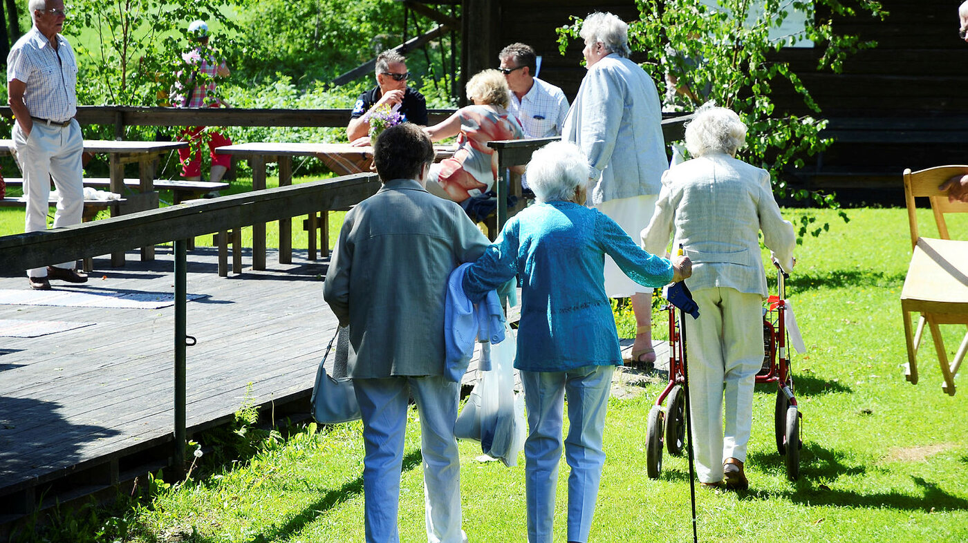 Eldre personer som går over en gressplen på vei til et arrangement. Noen har rullator.