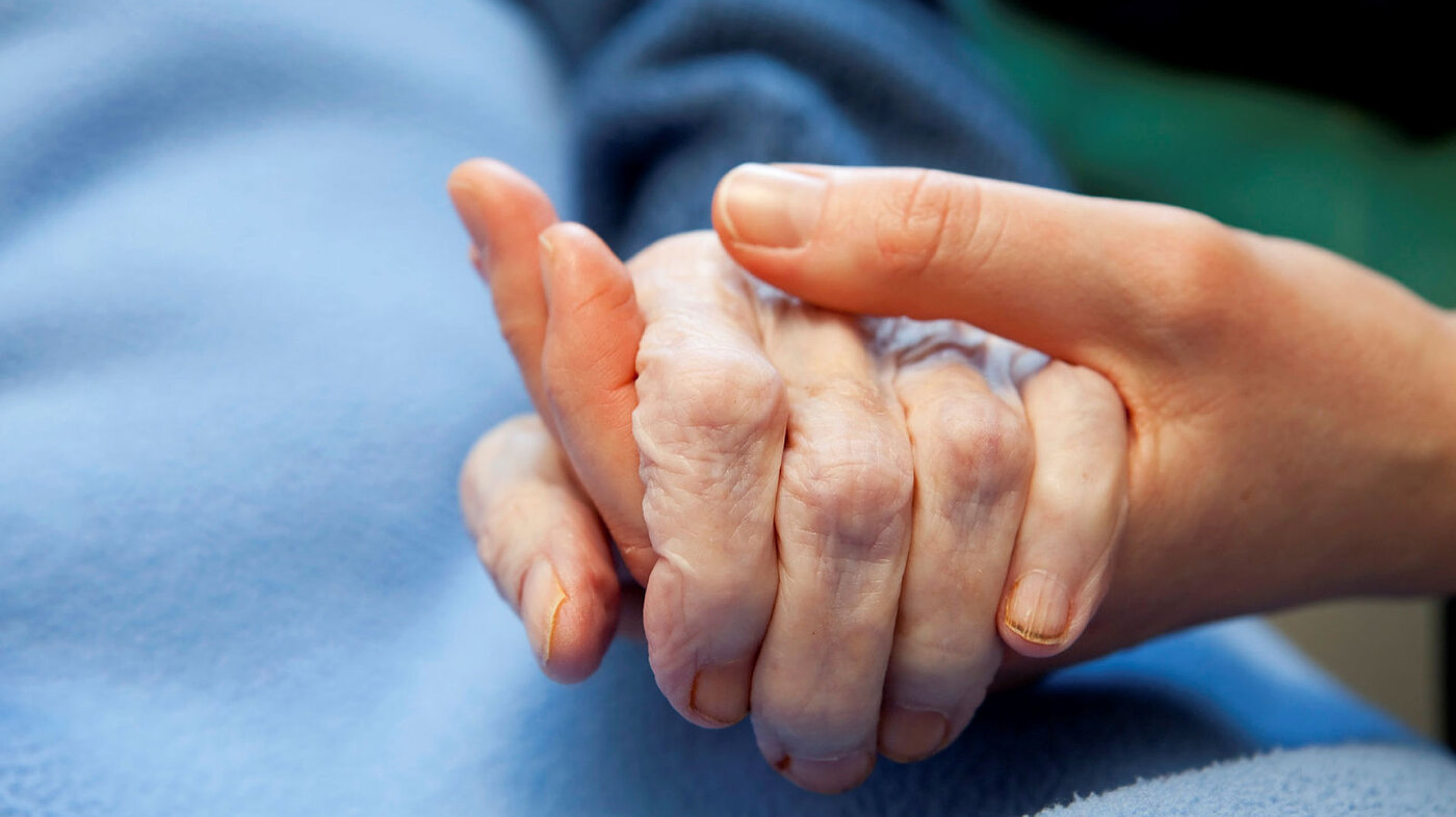 Bildet viser en gammel og en ung hånd som holder hender