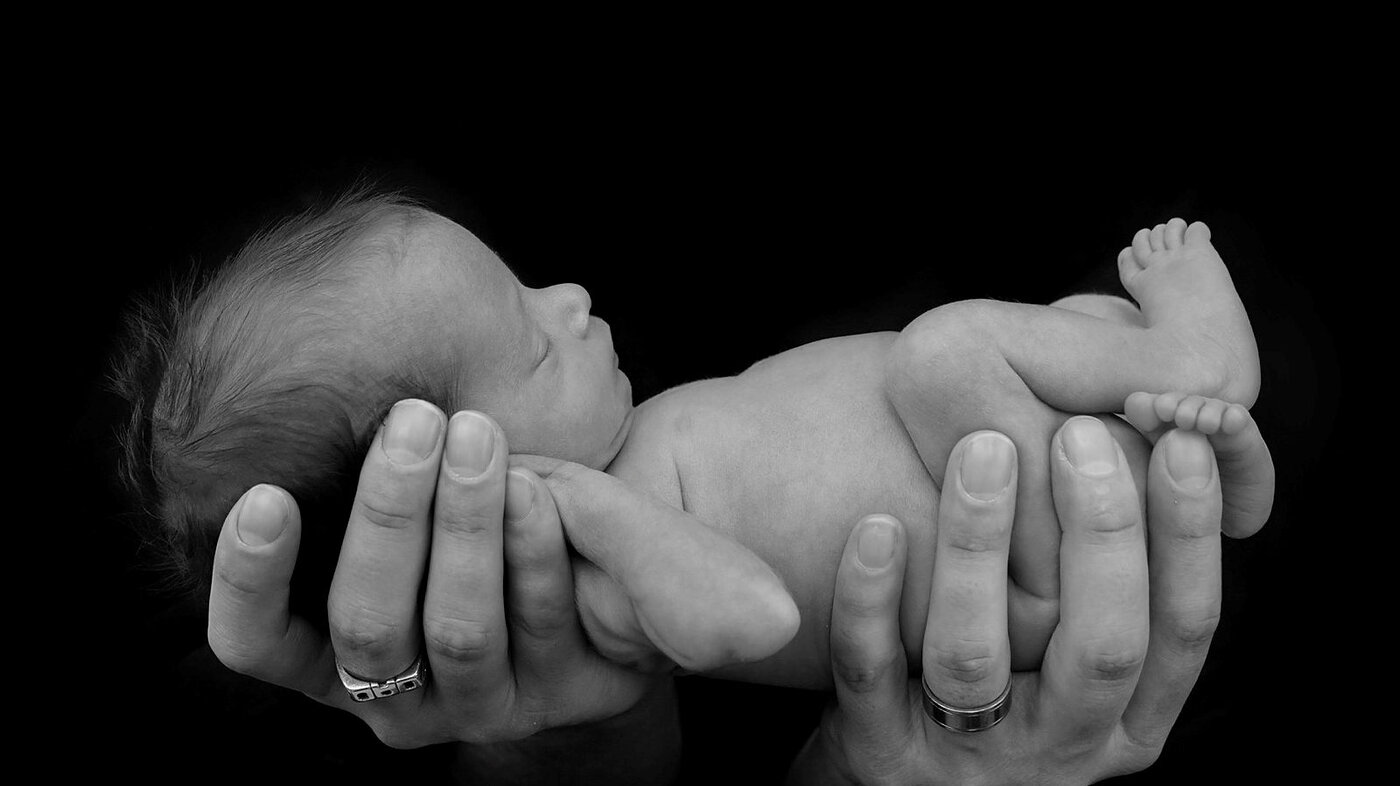 Et prematurt barn som holdes i sin fars hender.