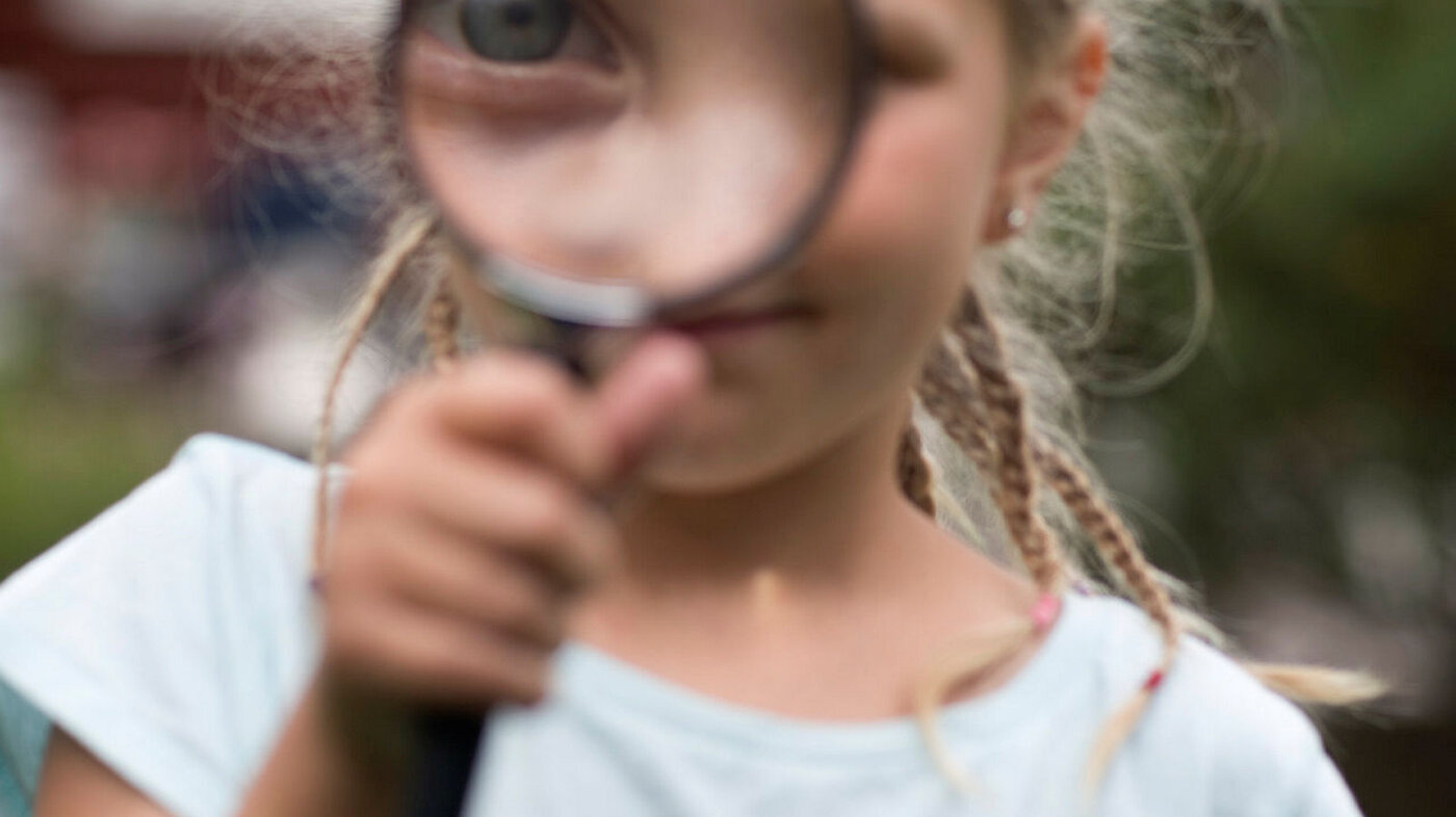 Bildet viser en jente som ser gjennom et forstørrelsesglass.
