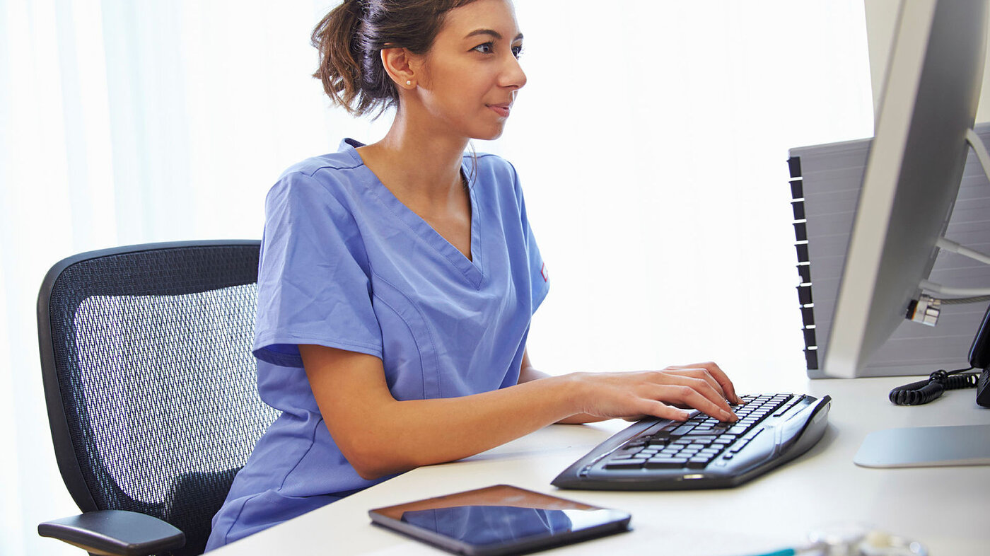 Bildet viser en kvinnelig sykepleier som skriver på et tastatur
