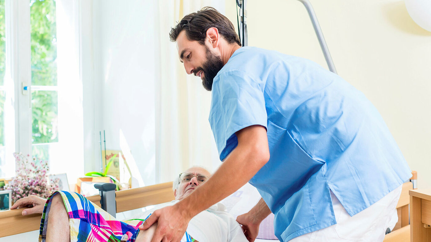 Bildet viser en eldre mann som blir stelt av en mannlig sykepleier.