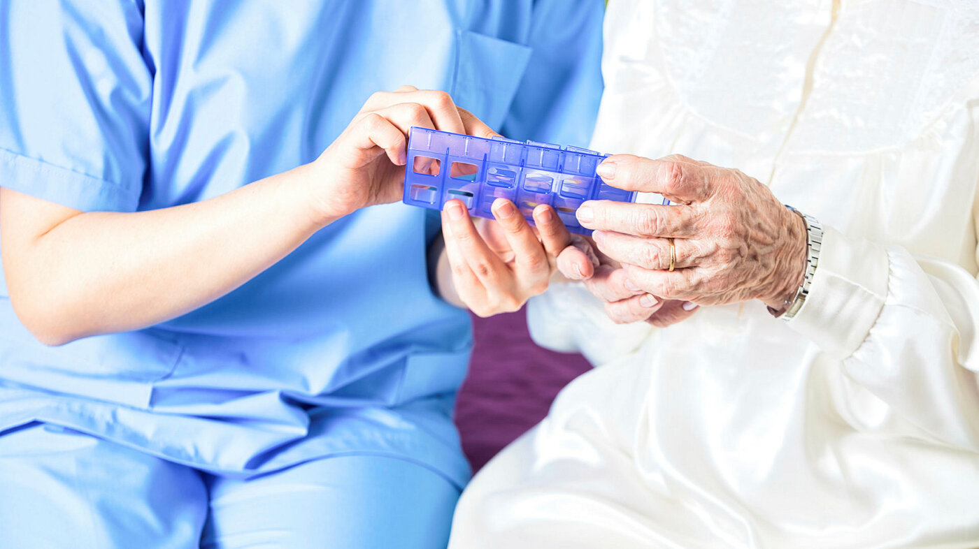 Bildet viser en sykepleier som viser en pasient en dosett med medisiner.
