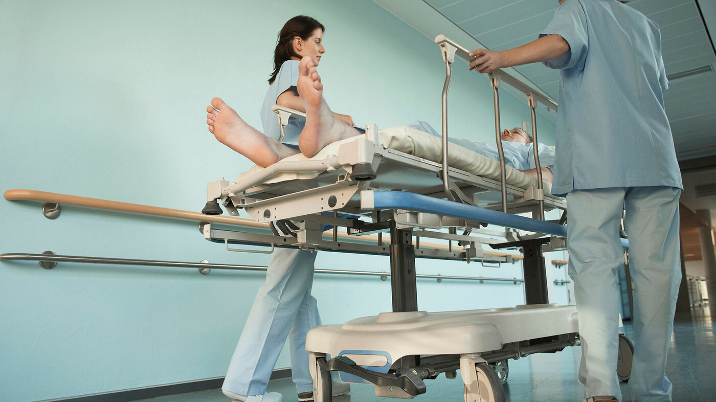 Bildet viser to sykepleiere med en pasient på en båre mellom seg.