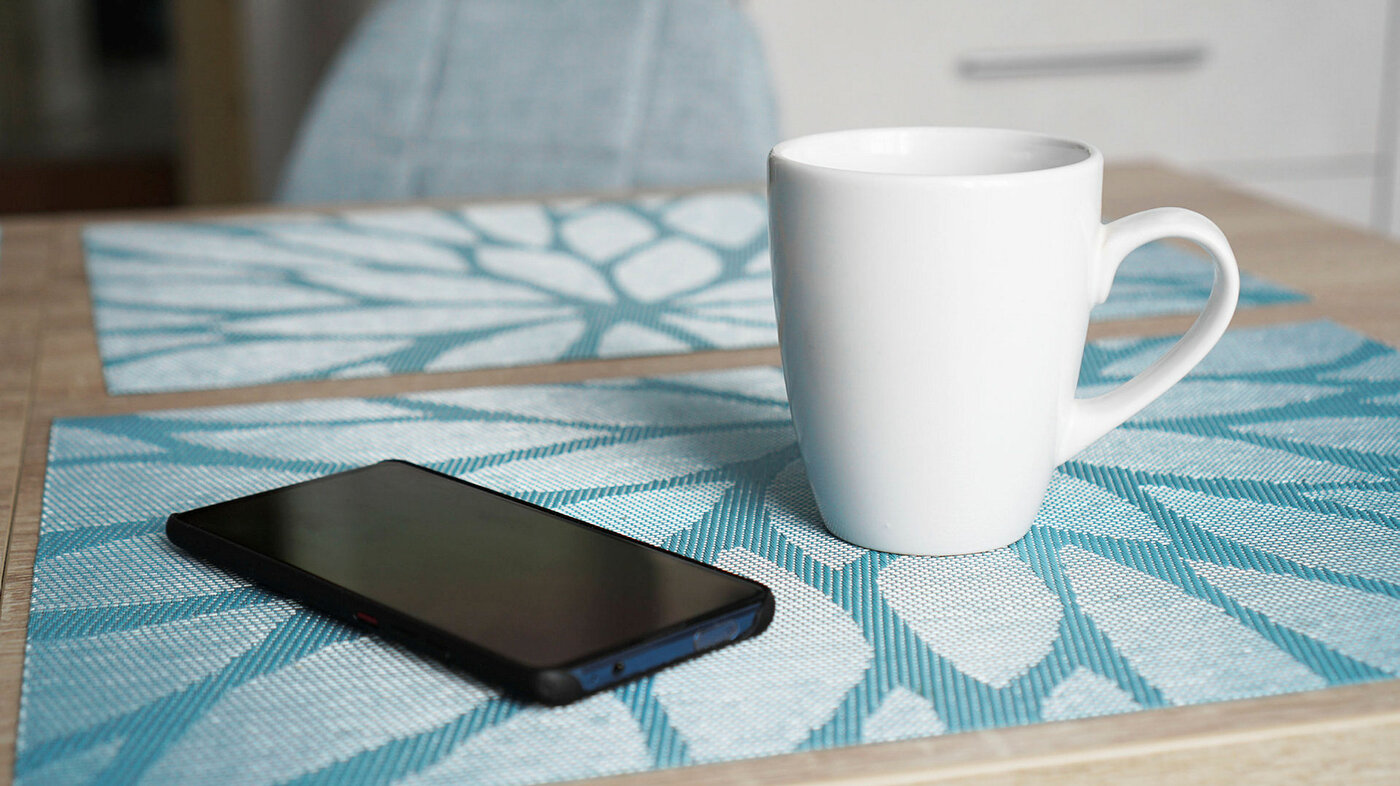 Mobiltelefon og kaffekopp på bord.