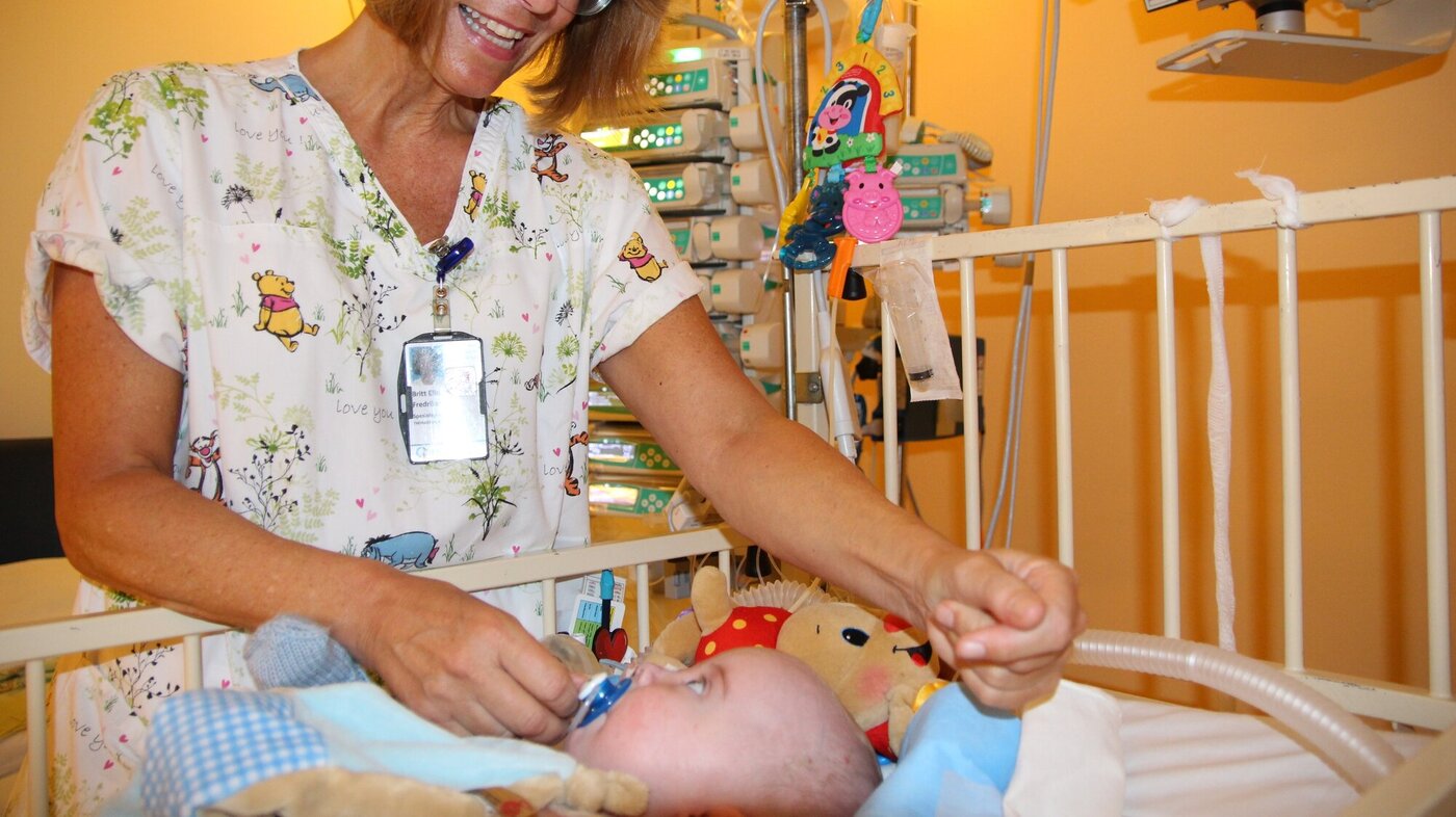 Bildet viser Britt Elin Fredriksen som kommuniserer med en liten baby som ligger i en sykehusseng.