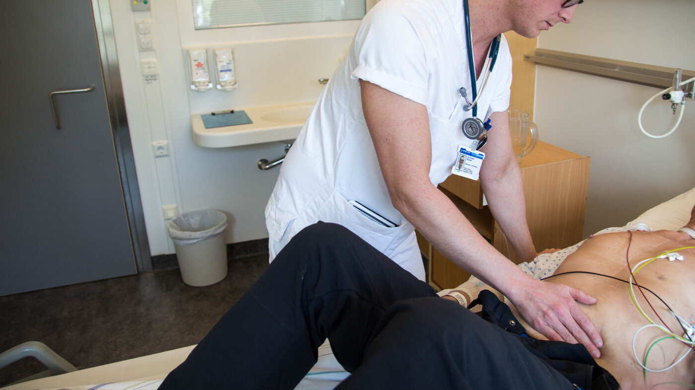 Bildet viser Jarl Robert Wexhall som palperer magen til en pasient.