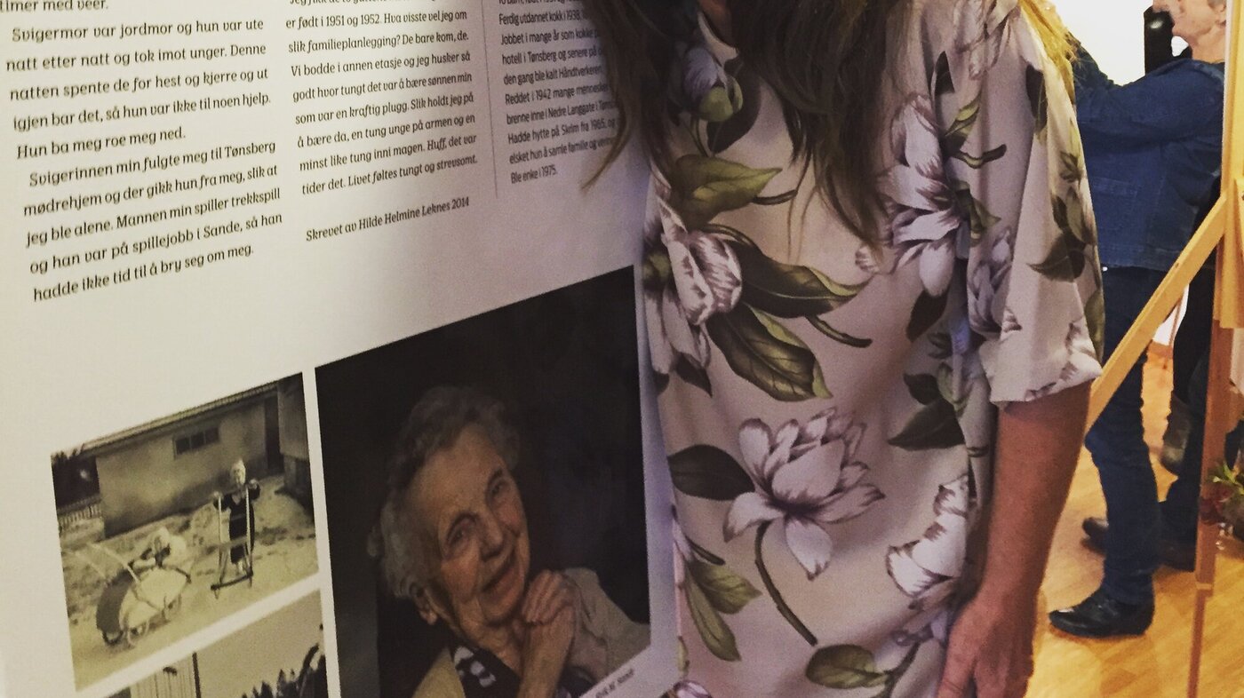 Bildet viser Hilde Helmine Leknes som holder rundt en av historiene som er stilt ut, plakat på staffeli.