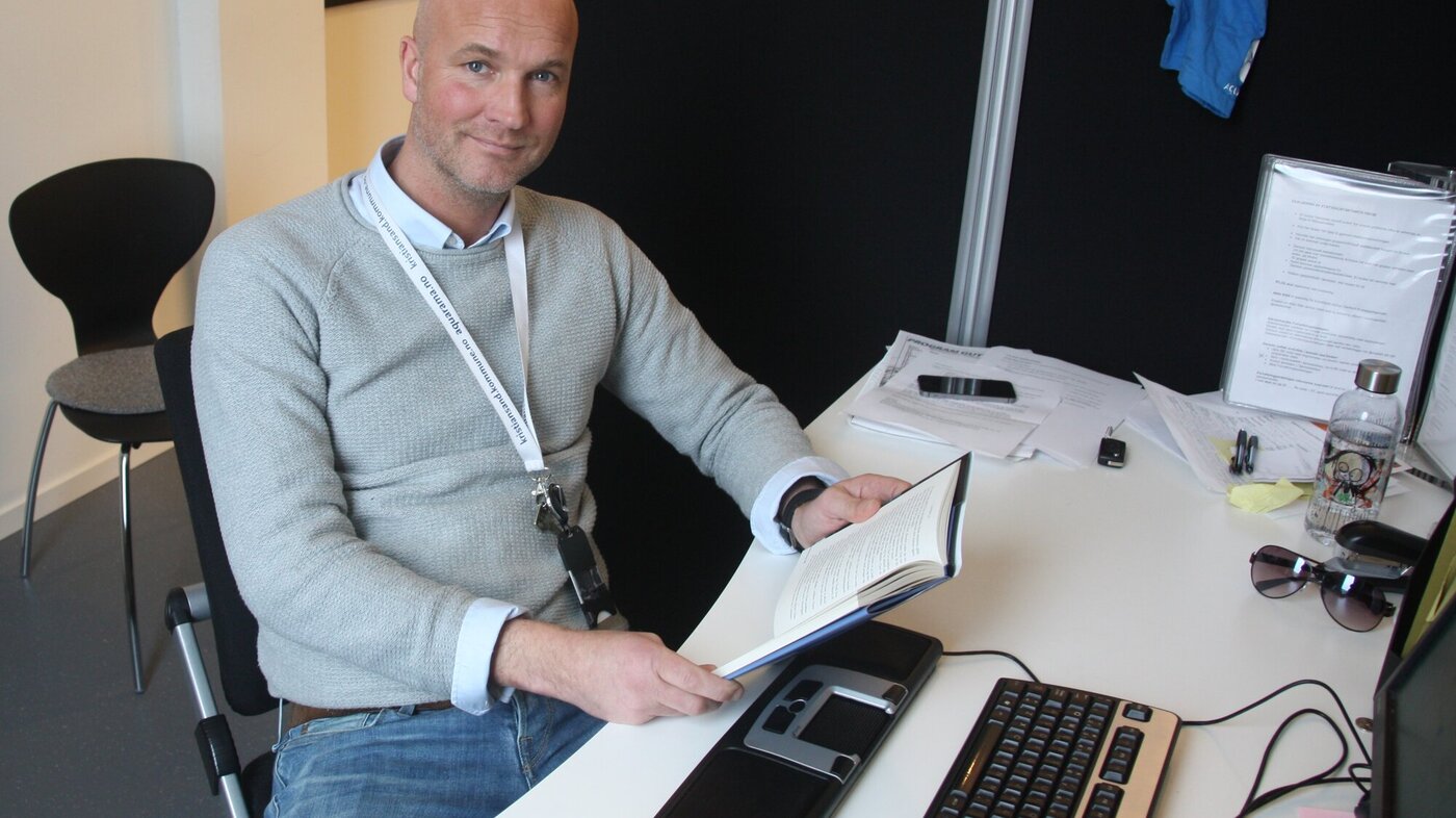 Bildet viser Jan-Erik Vik som sitter foran en datamaskin med bok i hånden.