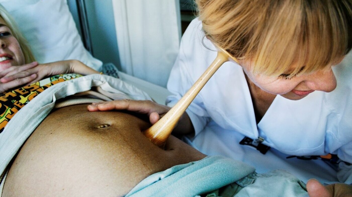 Bildet viser en jordmor som lytter på en mage med jordmorstetoskop.