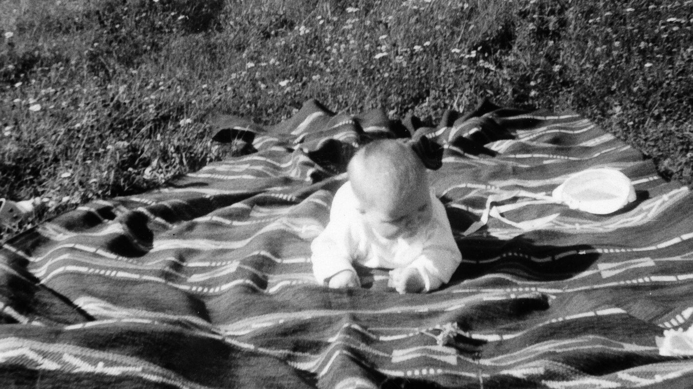 Bildet viser Karin Jonli som baby liggende på et teppe på gresset.