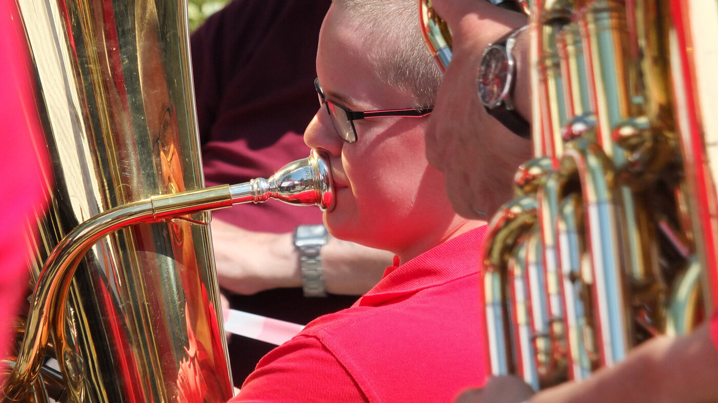 Nærbilde av gutt med kort hår og rød t-skjorte som spiller tuba i messingorkester