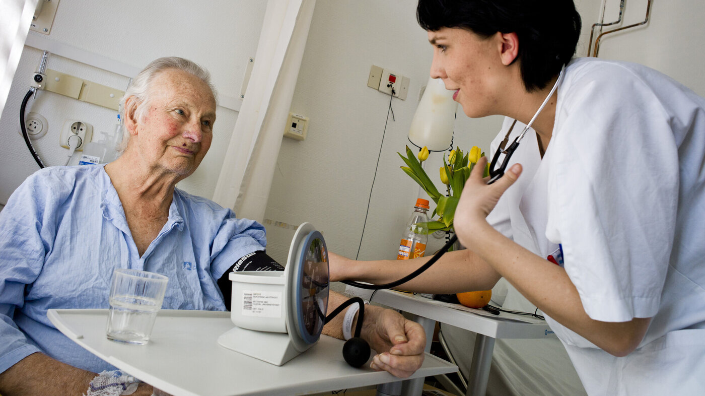 Bildet viser en sykepleier som sjekker blodtrykket til en pasient.