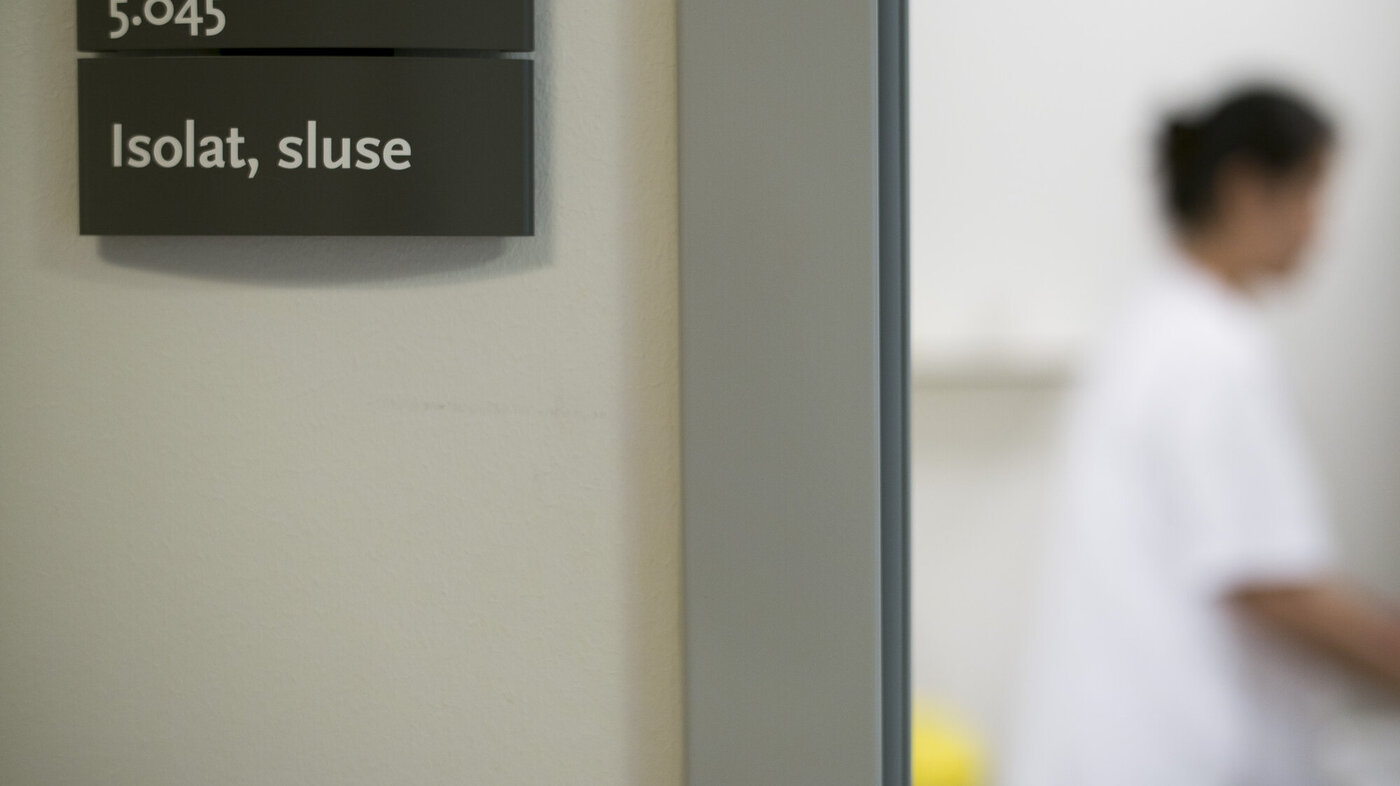 Bildet viser et skilt der det står isolat, sluse og gjennom et vindu i døren skimtes en sykepleier