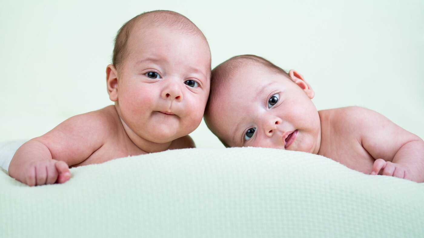 To nyfødte barn som ligger på teppe og kikker rett inn i kamera.