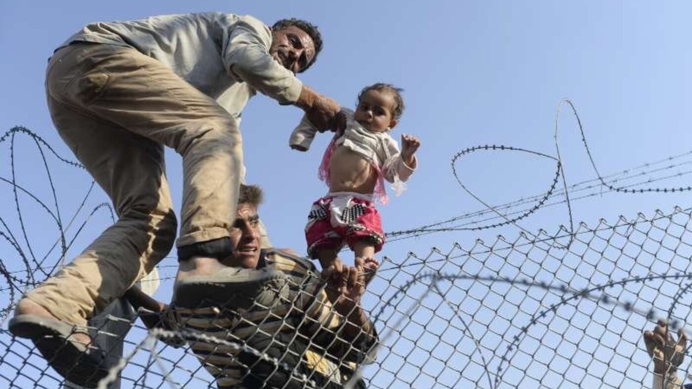 Syriske flyktinger klatrer over piggtrådgjerde for å kommer til Tyrkia