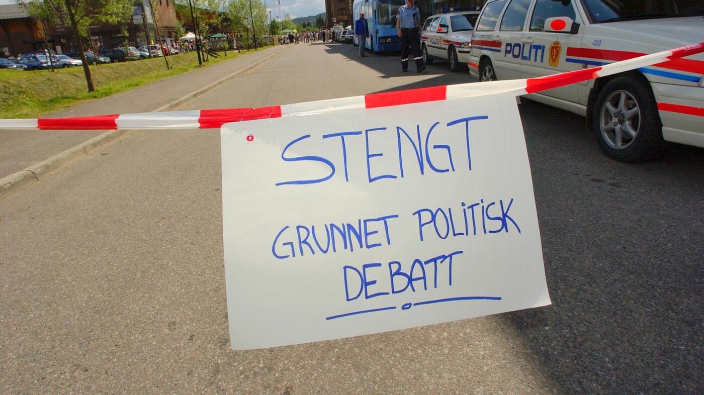 Bildet viser en avsperret vei med et skilt hvor det står "Stengt på grunn av politisk debatt"
