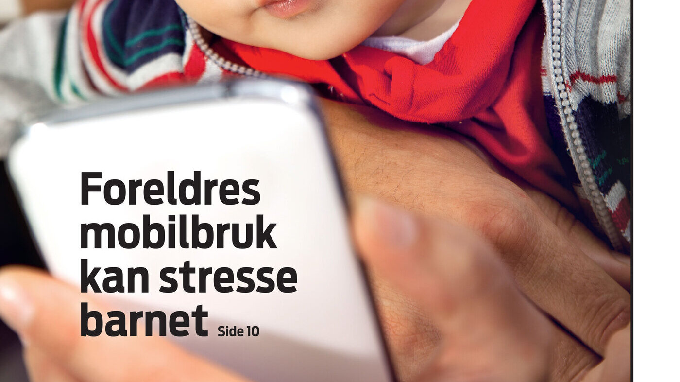 En baby sitter på fanget til en forelder og ser på mobilen.