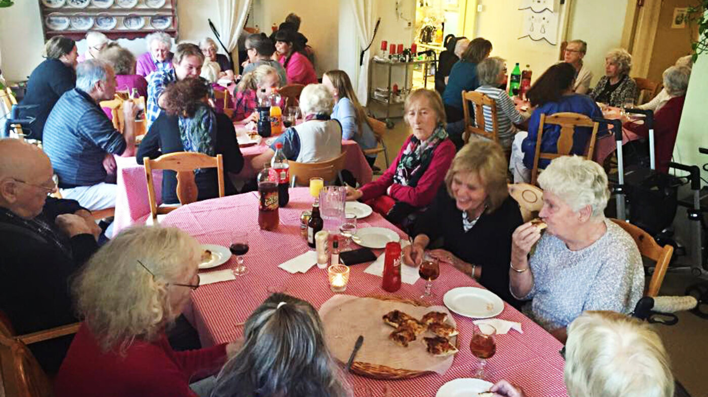 Folk sitter rundt bord og spiser pizza og har quiz. 