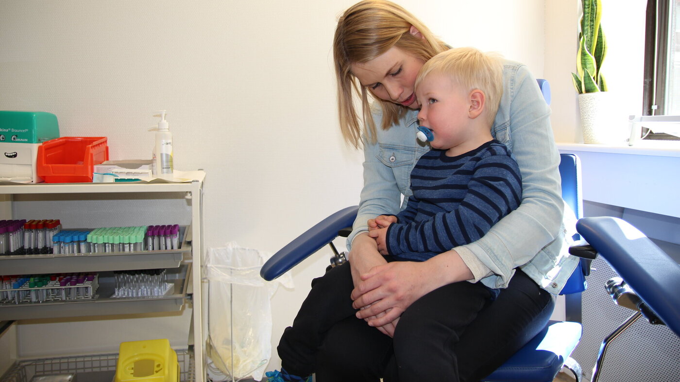 Sebastian sitter på mammas fang og venter på blodprøve.