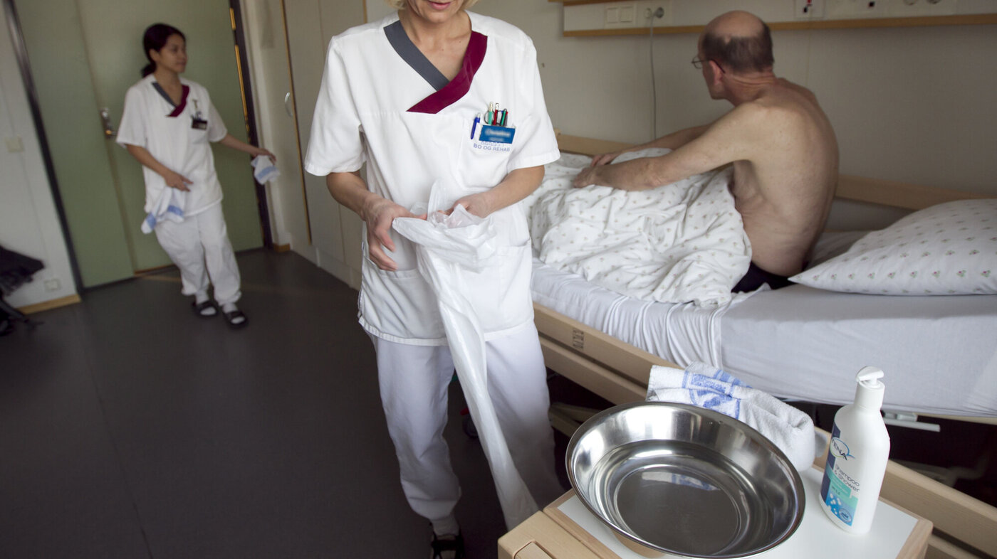 Bildet viser to helsefagarbeidere som skal vaske en pasient som ligger i en seng
