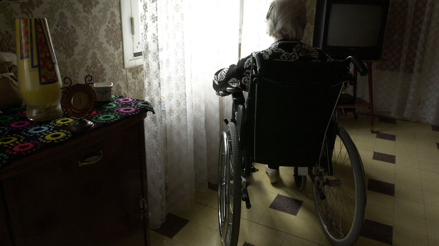 Sykehjemsbeboer i rullestol som sitter alene foran vindu