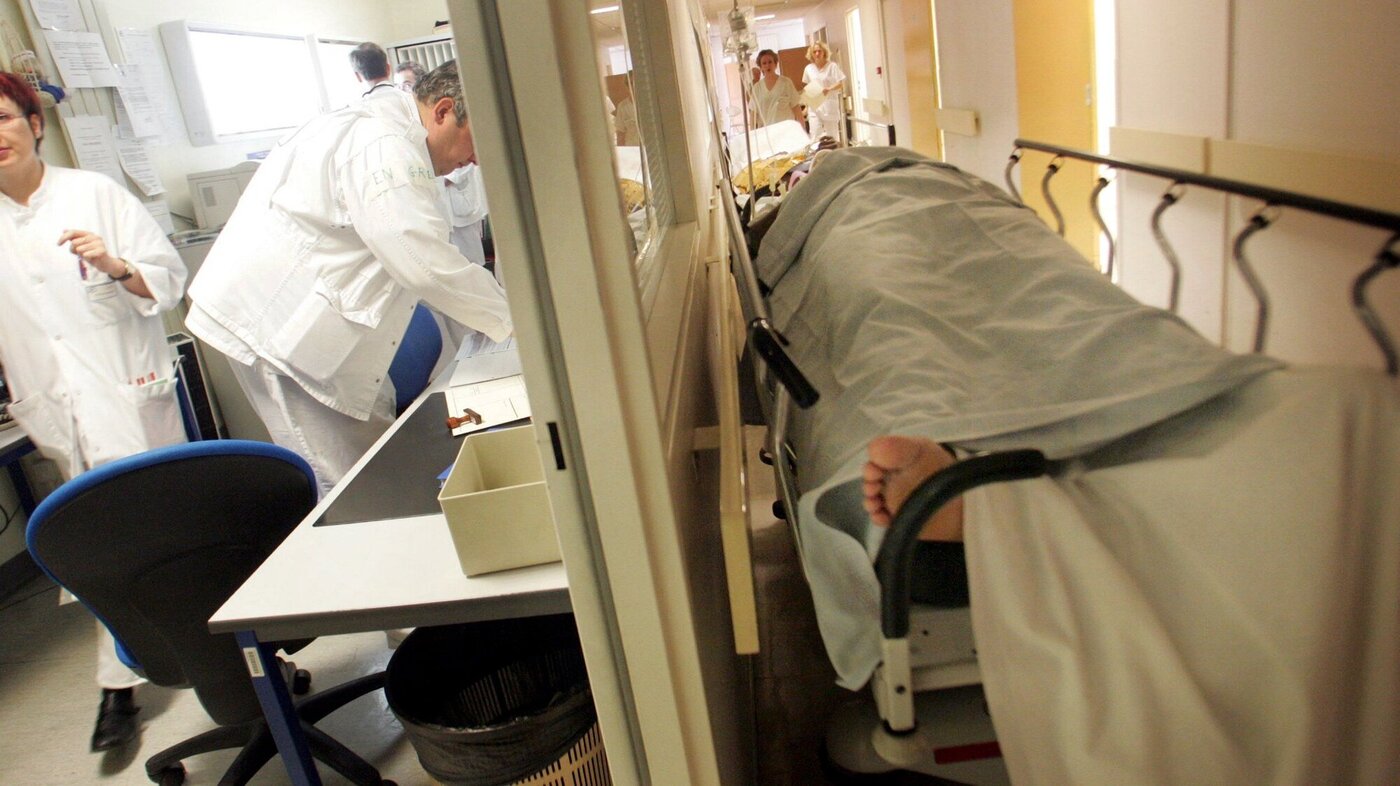 Bildet viser korridorpasient på sykehus. Helsepersonell jobber i bakgrunnen