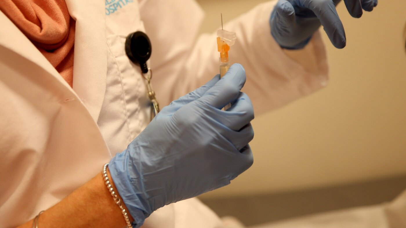 Bildet viser en to hender med hansker som gjør klar en vaksine.
