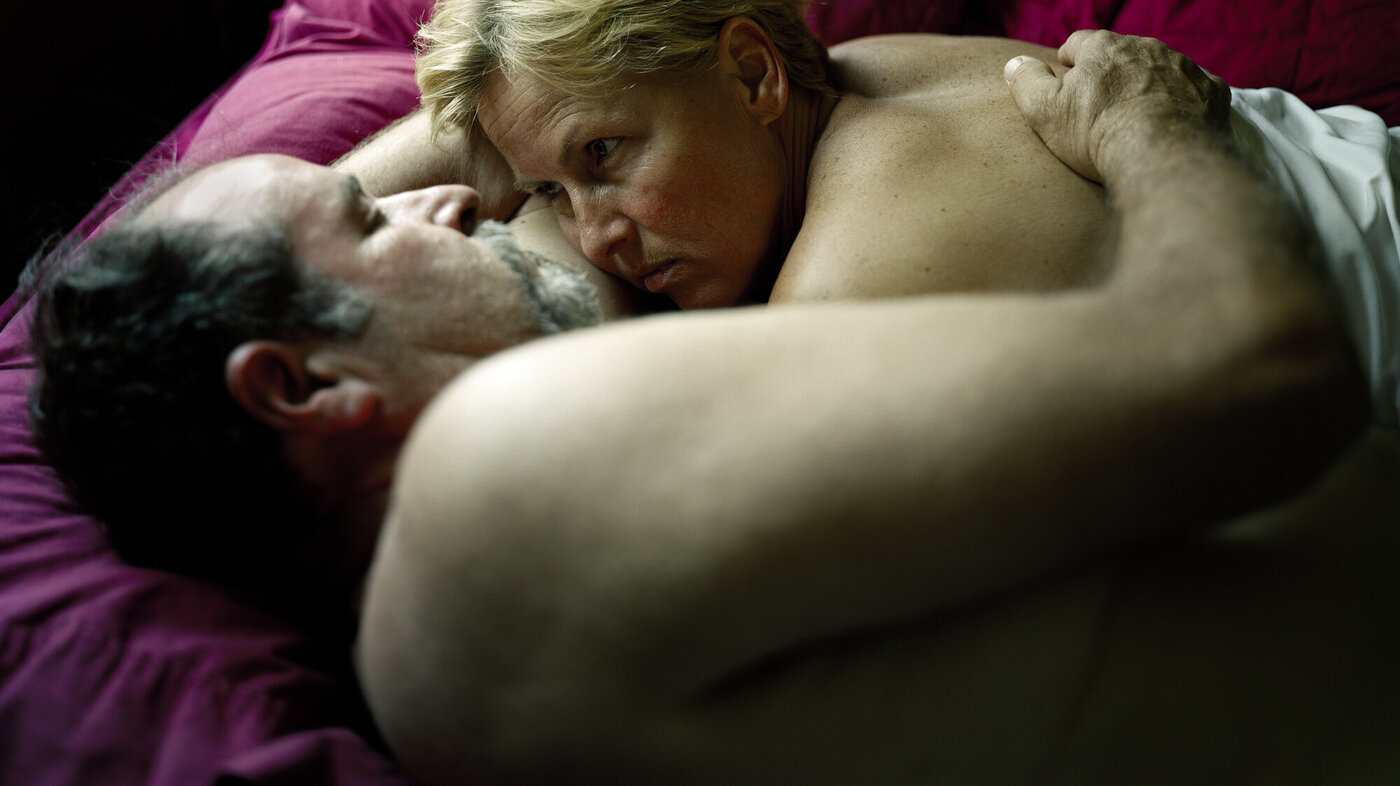 Et voksent par ligger i sengen halvveis under dyna og ser på hverandre