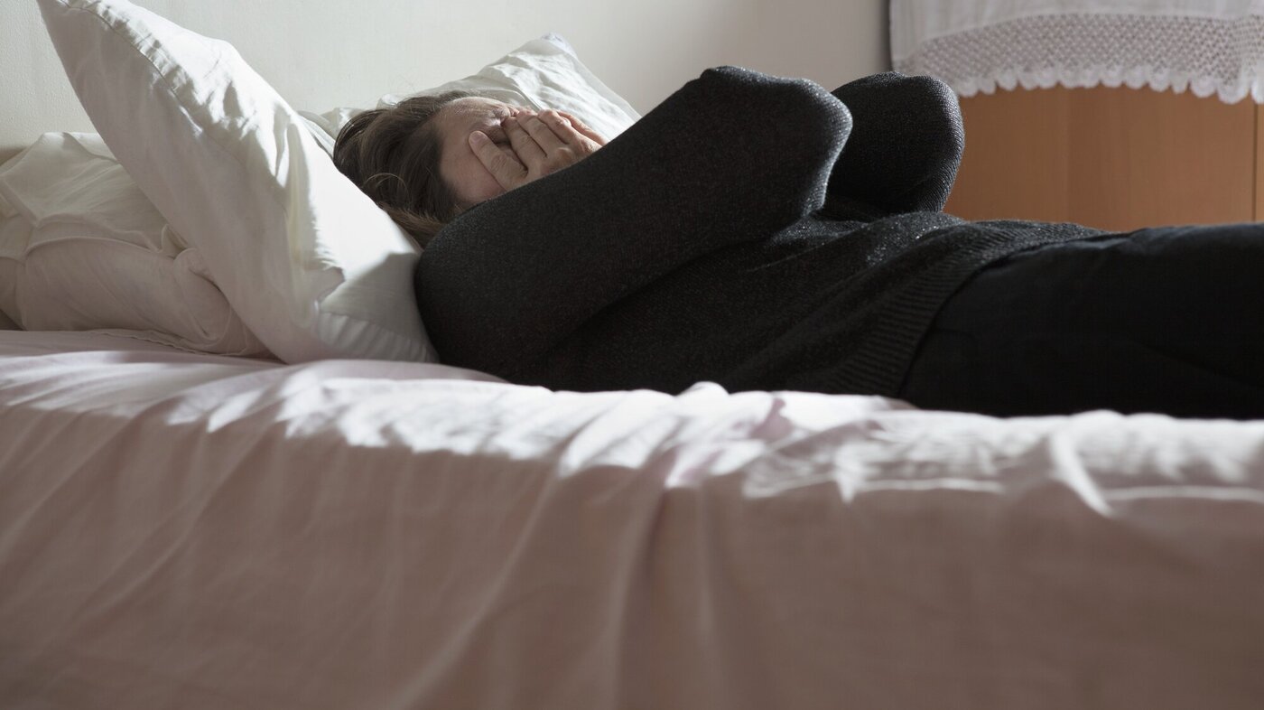 Bildet viser en deprimert kvinne som ligger på en seng og holder hendene foran ansiktet