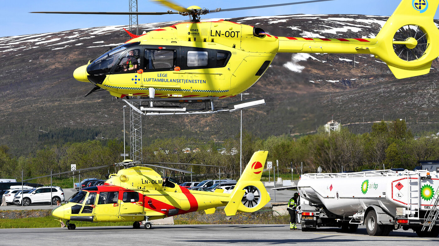 Bildet viser et ambulansehelikopter som er i ferd med å lette, og et som står på bakken i bakgrunnen