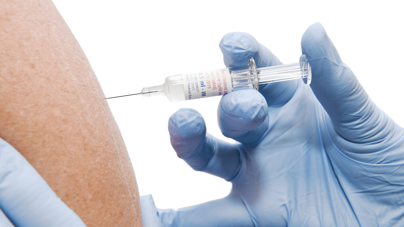 Bildet viser hender med hansker som skal til å sette en vaksine i en arm.
