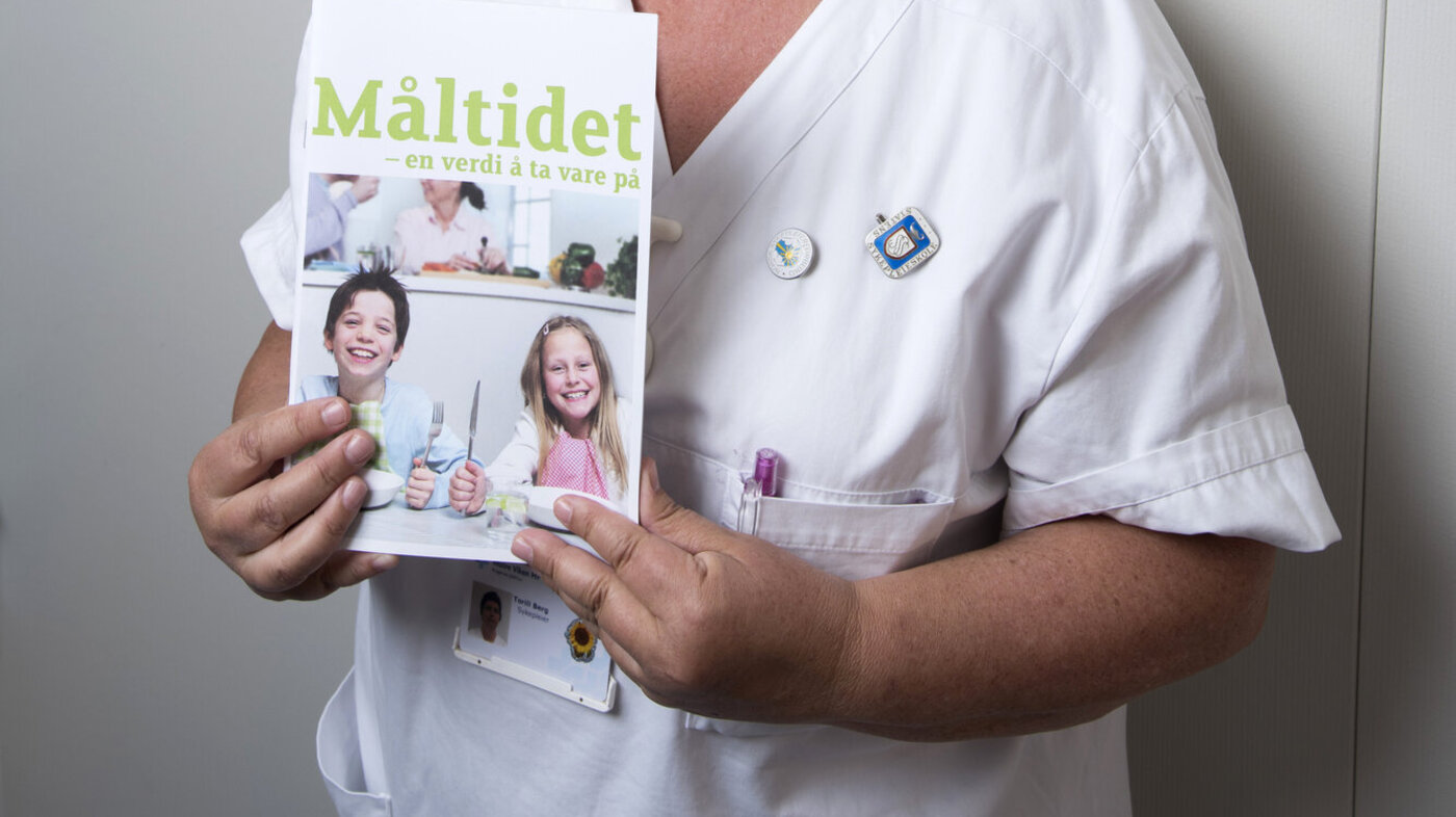 Torill Berg poserer med bladet "Måltidet", under høydemålingsstativ ved overvektsklinikken.