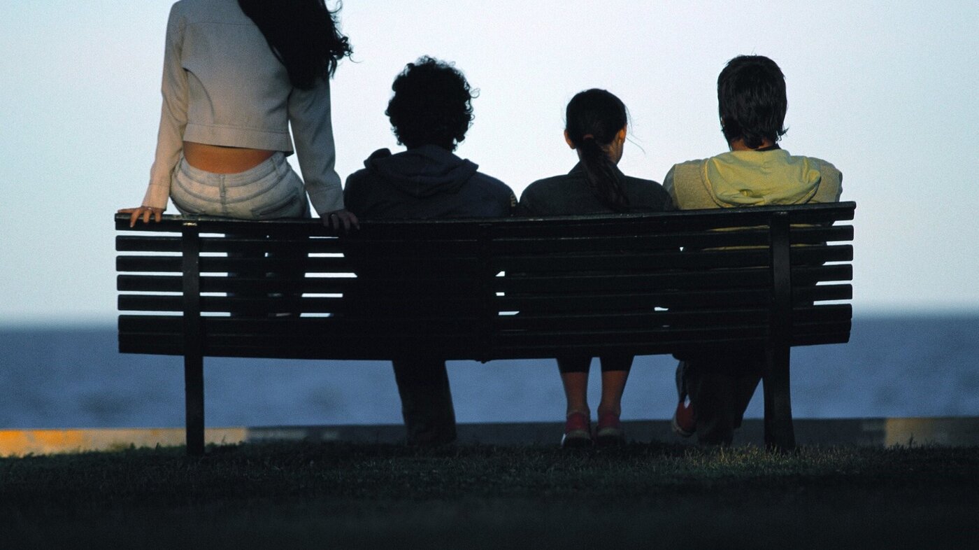 Fire ungdommer som sitter på en benk med ryggen til kamera og ser utover