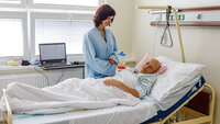 Bildet viser en kvinne som står ved sengen til en døende kvinnelig kreftpasient