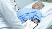 Bildet viser en mann i en sykehusseng. En sykepleier står ved siden av med et skjema i hånden