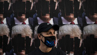 Bildet viser en mann med maske som det står Biden på, foran nedtusjete plakater av Trump.