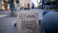 Bildet viser Karl Johans gate og en plakat som en sittende mann har foran seg, hvor det er bønn om bidrag til en som har det vanskelig.