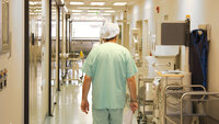 Bildet viser ryggen på en helsearbeider som går nedover en korridor på sykehus.