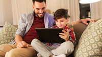 Bildet viser et barn som ser på et nettbrett sammen med sin far