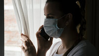 Sykepleier med munnbind kikker ut av vindu