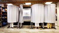 Bildet viser stemmegivere bak forheng i et valglokale.